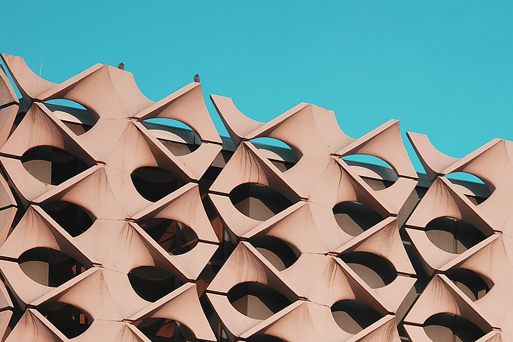 Nahaufnahme der Fassade der Stadthalle Chemnitz mit wiederkehrenden geometrischen Betonelementen vor blauem Himmel.