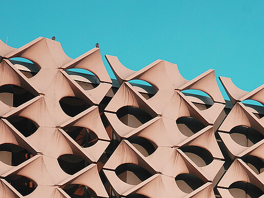 Nahaufnahme der Fassade der Stadthalle Chemnitz mit wiederkehrenden geometrischen Betonelementen vor blauem Himmel.