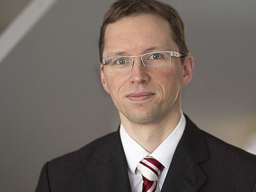 Stefan Kornhuber in a suit with tie and glasses smiles into the camera.