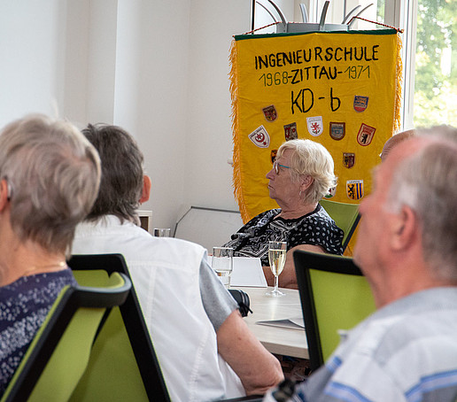 Ältere ehemalige Studierende sitzen an einer Tafel im Senatssaal. Im Hintergrund ist ihre Klassenfahne zu sehen. 