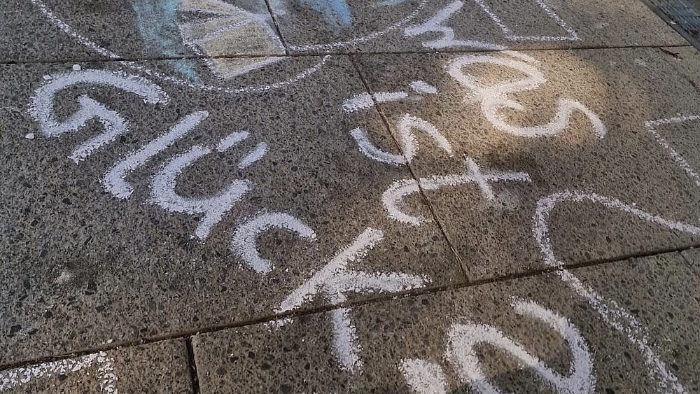 Kreidezeichnungen auf dem Asphalt mit dem Schriftzug "Was ist Glück?".