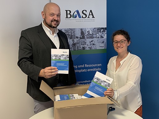 Prof. Matthias Schmidt and BASA employee Katharina Roitzsch hold the new BASA information materials up to the camera and smile.