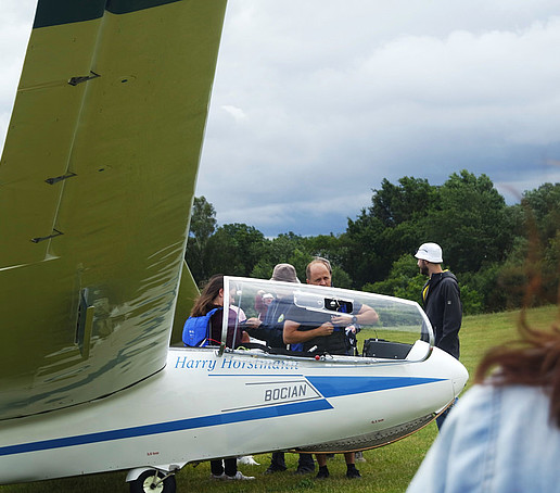 Rumpf und Flügel eines Ultraleichtflugzeuges auf dem Görlitzer Flugplatz. Studierende versammeln sich drumherum.