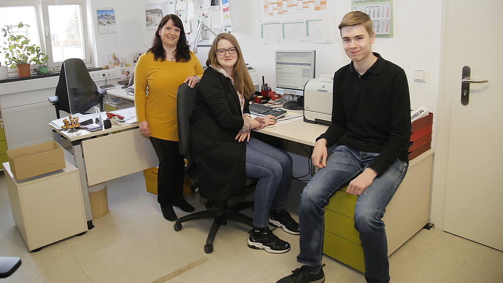 Two trainees and their training supervisor sit in the office and smile at the camera.