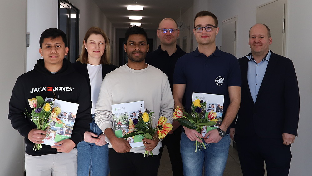 Die Facharbeiter, Kristin Groß, Udo Johne und Christoph Duscha stehen im Gang des Hochschulgebäudes und lächeln in die Kamera.