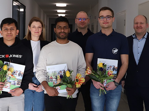 Die Facharbeiter, Kristin Groß, Udo Johne und Christoph Duscha stehen im Gang des Hochschulgebäudes und lächeln in die Kamera.