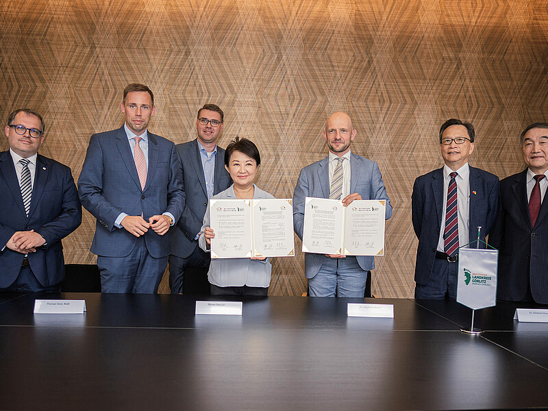 Representatives from the district of Görlitz, Taiwan and the HSZG stand next to each other in a meeting room and smile into the camera, while the district administrator and the Taiwanese representative hold the signed memorandum in front of them.