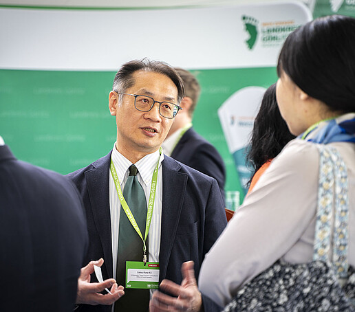 Lian-Ruey Ke talking to conference participants in front of a green information stand.