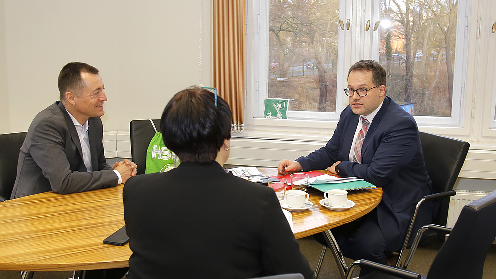 Bundestagsabgeordneter Herbst, Frau Schütz und der Rektor sitzen am Tisch bei einer Besprechung.