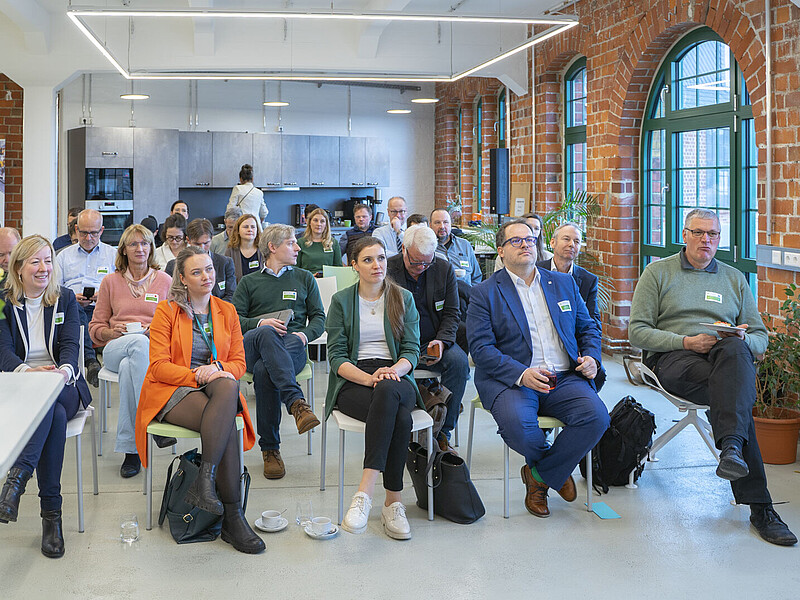 Workshop-Teilnehmende sitzen auf Stühlen im einem Raum mit roten Steinwänden und richten ihren Blick in Richtung Vortragenden.
