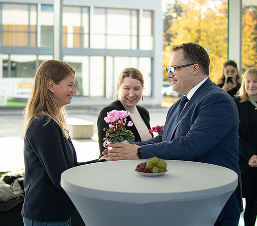 The rector hands over a potted plant to a professor.
