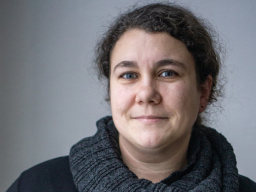 Kim Schwarz wears a dark sweater with her dark curls tied back and smiles at the camera.