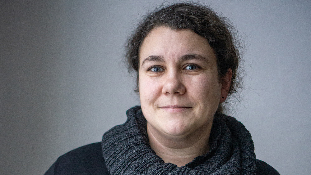 Kim Schwarz wears a dark sweater with her dark curls tied back and smiles at the camera.