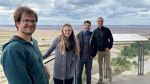 Vier Personen stehen auf einer Aussichtsplattform des Tagebaus Nochten und lächeln in die Kamera.