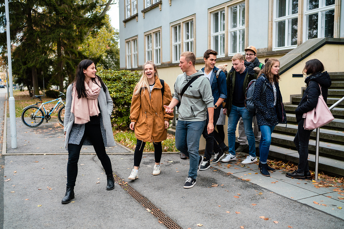 A group of cheerful young people come out of a university building.
