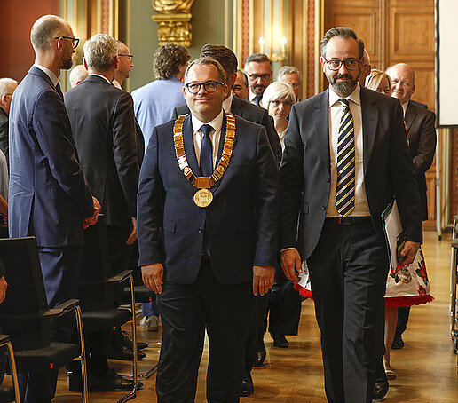 The procession of honor, led by the Rector and the Minister of Science, solemnly leaves the Bürgersaal to a standing audience.
