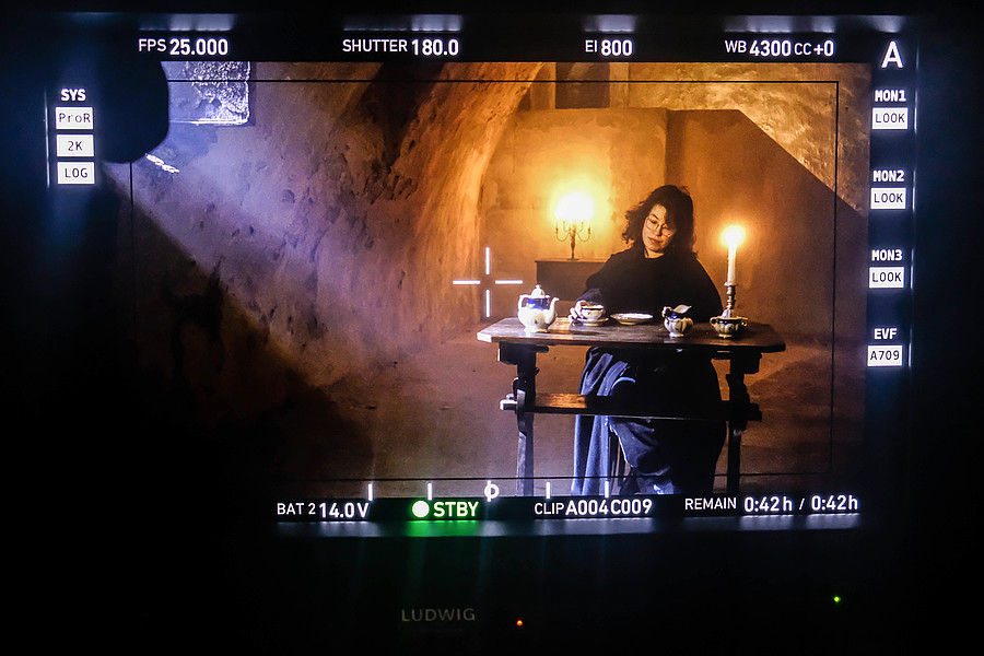 Kameraausschnitt, der eine Frau im Kellergewölbe sitzend an einem Tisch zeigt.