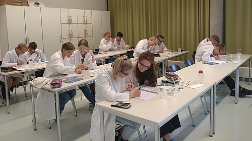 Schülerinnen und Schüler sitzen experimentierend im Labor