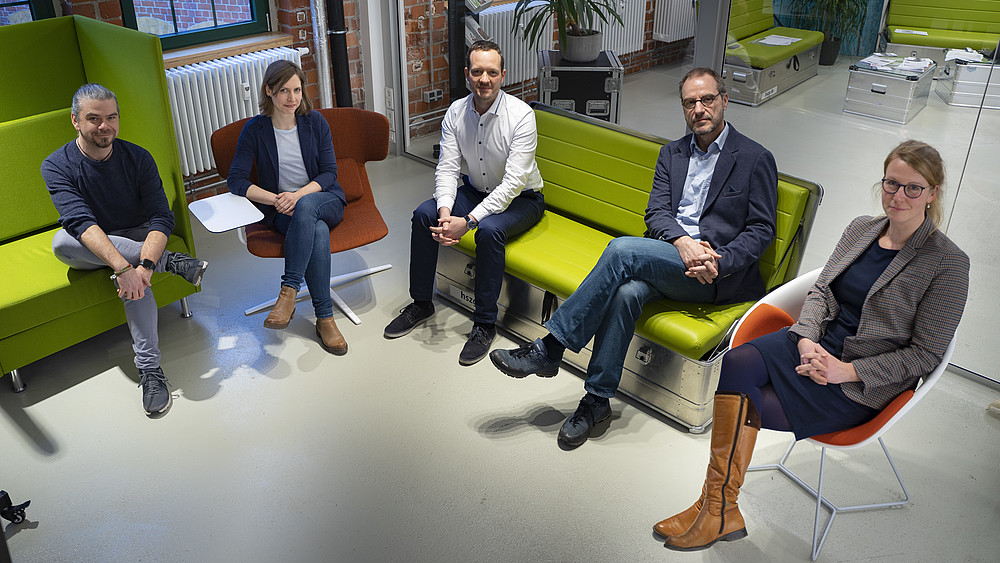 The Life and Technology team sits in a semicircle in the rooms of the co-creation lab at Celsiuz and smiles at the camera.
