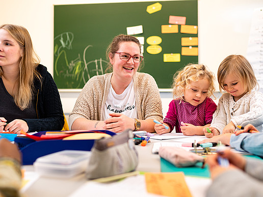 Teachers and children at the table, in the background a green board with slips of paper.
