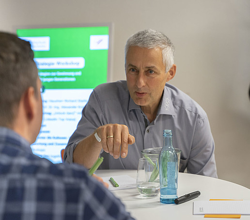 Two participants sit at the table and tell each other something.