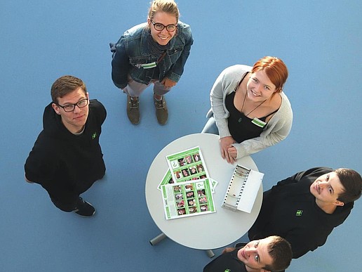 Five contact persons for prospective students stand around a bar table and are photographed from above