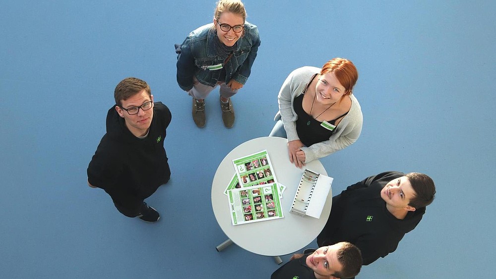 Five contact persons for prospective students stand around a bar table and are photographed from above