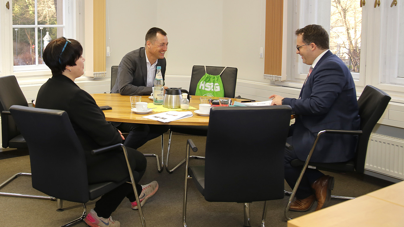 Bundestagsabgeordneter Herbst, Frau Schütz und der Rektor sitzen am Tisch bei einer Besprechung.