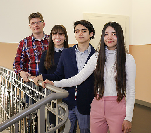 Three Mexican students and their project manager stand one behind the other in a corridor and look into the camera.
