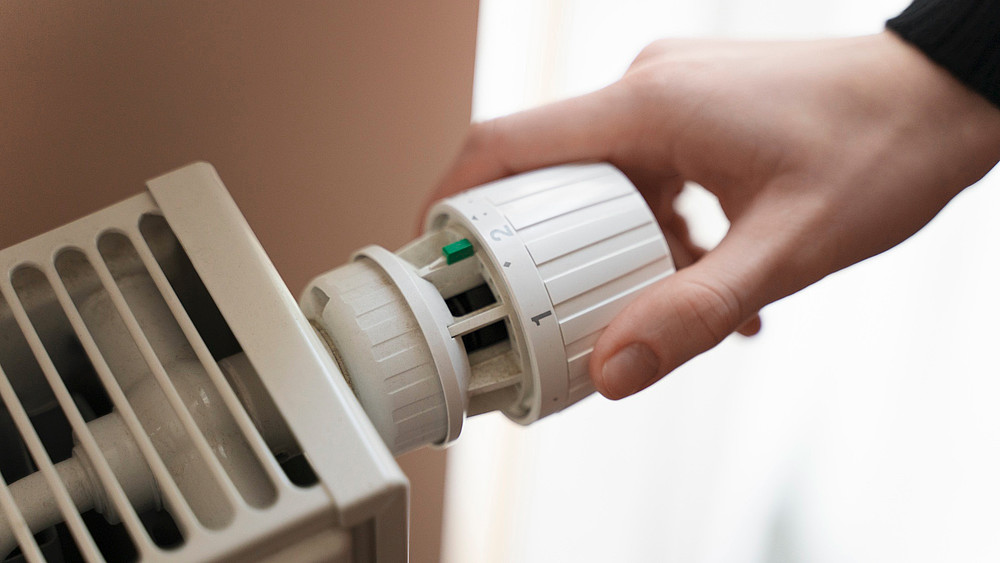 A hand screws on the control of a radiator.
