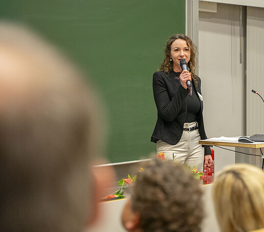 A woman speaks into a microphone in front of the audience.