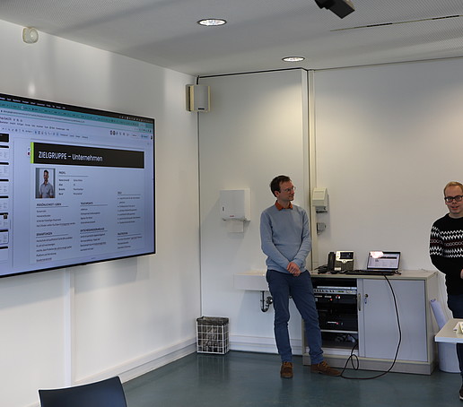Workshop participants stand in front of a large monitor in the seminar room.