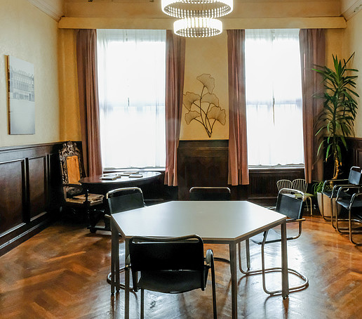 Ein historisch anmutender Raum, in dem ein sechseckiger Tisch mit Stühlen steht, an den Wänden sieht man Holzvertäfelung.