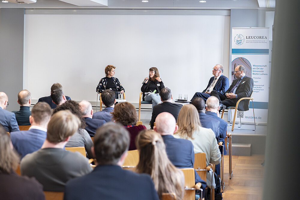 Podium mit 4 Personen vor Zuschauern