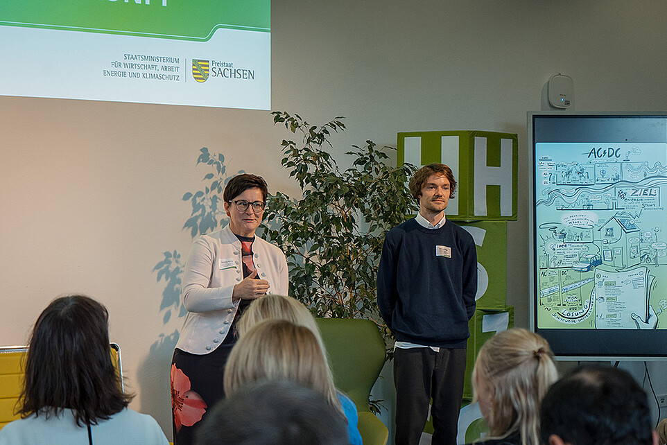Two futureSAX employees speak to an audience in the auditorium.