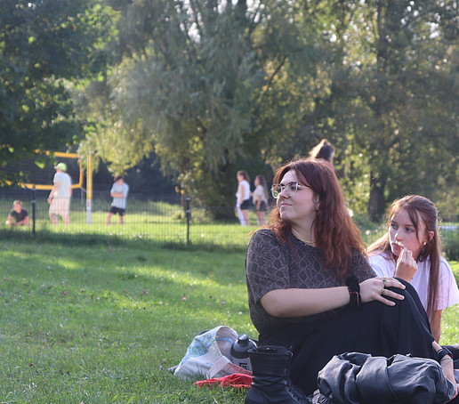 Female students sit on a picnic blanket in a meadow.