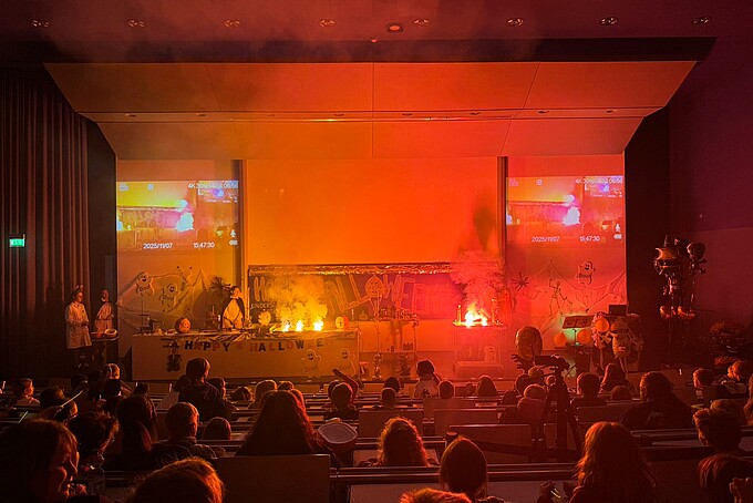 The stage lights up in red. The children's audience looks towards the stage in amazement.