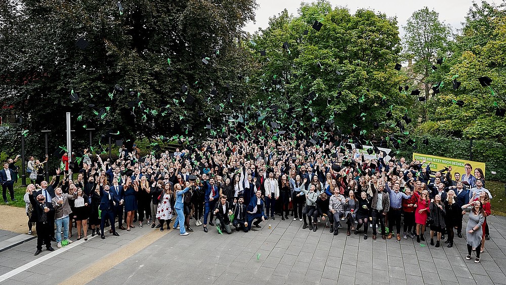 Absolvent*innen auf dem Campus werfen die Absolventenhüte in die Luft.