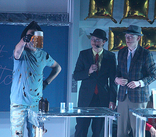 Performers experiment with a beer on stage.