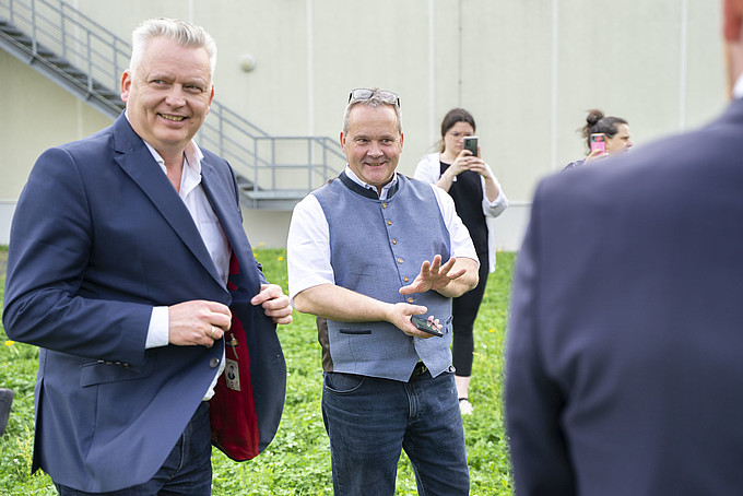 Zwei Menschen in legerer Geschäftskleidung führen ein Gespräch im Freien, ihre Lächeln deuten auf einen informellen und freundlichen Austausch hin.