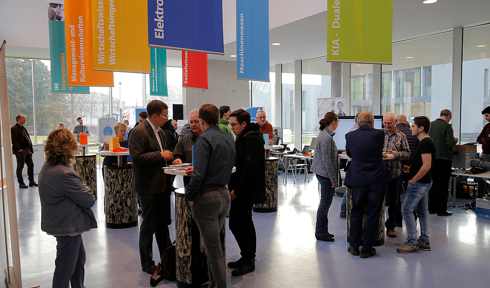 Studieninteressierte und Hochschulangehörige stehen an Beratungstischen im Foyer des Peter-Dierich-Hauses in Zittau.