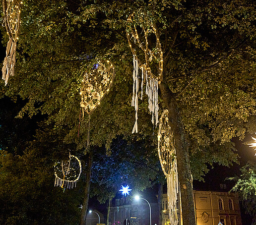 Dream catchers embroidered with lights hang in a tree.
