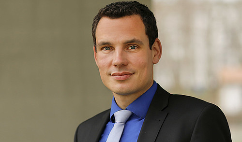 Profilfoto von Prof. Dr. iur. Erik Hahn gekleidet in einen schwarzen Anzug mit dunkelblauen Hemd und einer Krawatte. 
