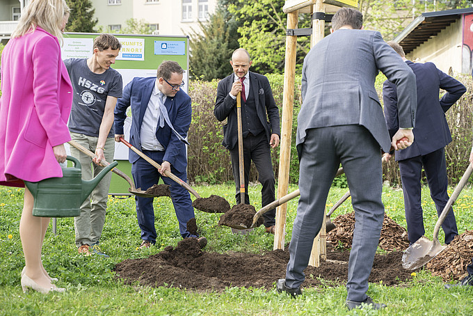 Gruppe von Personen nimmt aktiv an einer Baumpflanzzeremonie teil, arbeitet gemeinsam daran, ein Loch im Freien mit Erde zu füllen.