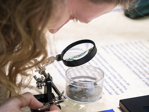 A student looks through a magnifying glass into a glass dish filled with a sample.