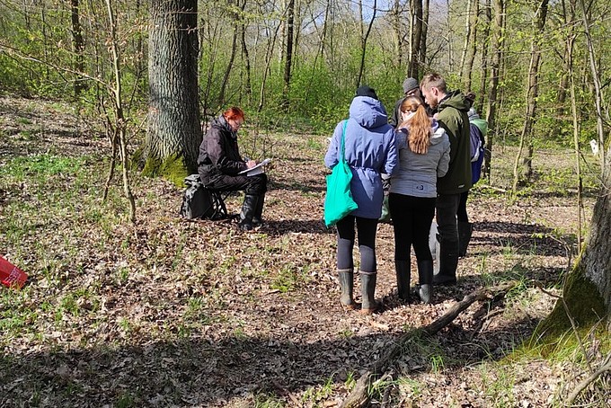 Professor Heidger sits on a meadow in the forest surrounded by students.