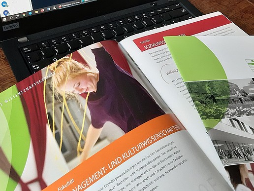 Image brochure of the HSZG, with the page of the Faculty of Management and Cultural Studies open. Brochure lying on the keyboard of a laptop.