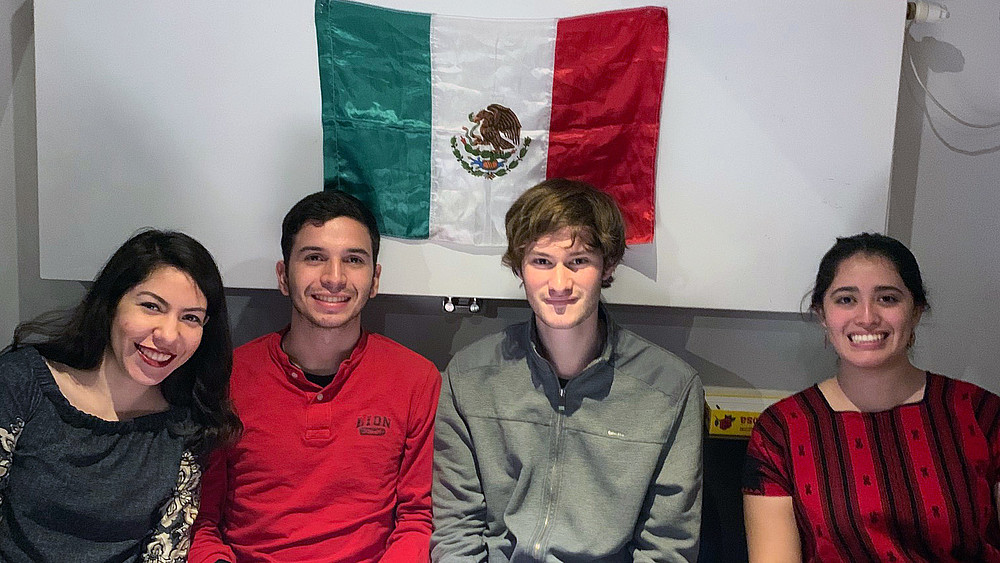 Vier Studierende sitzen vor einer mexikansichen Flagge.