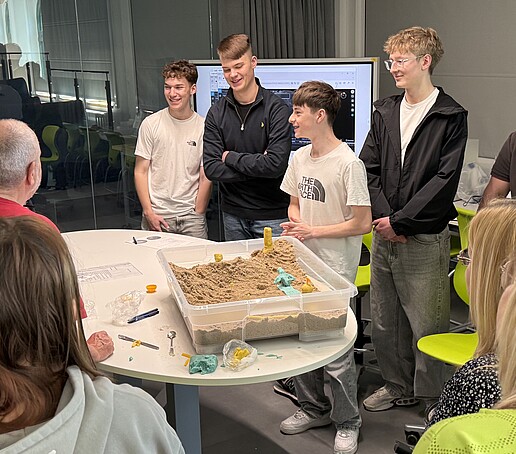 Schülerinnen und Schüler stehen um einen Tisch herum.