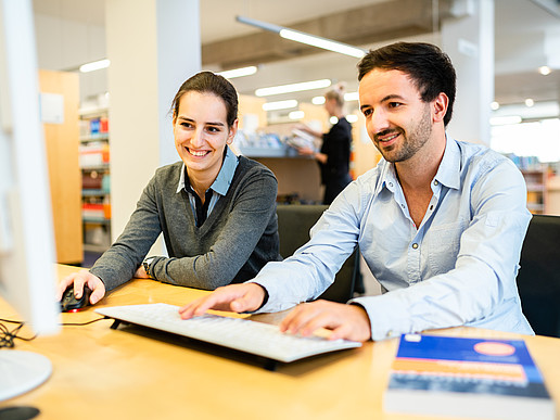 Zwei Studierende (männilich und weiblich) sitzen vor einem Computerbildschirm